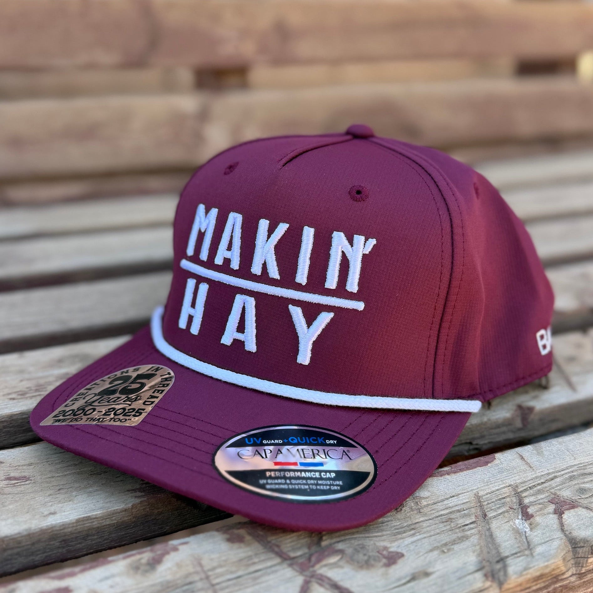 Maroon cap with 'MAKIN HAY' text on a wooden surface