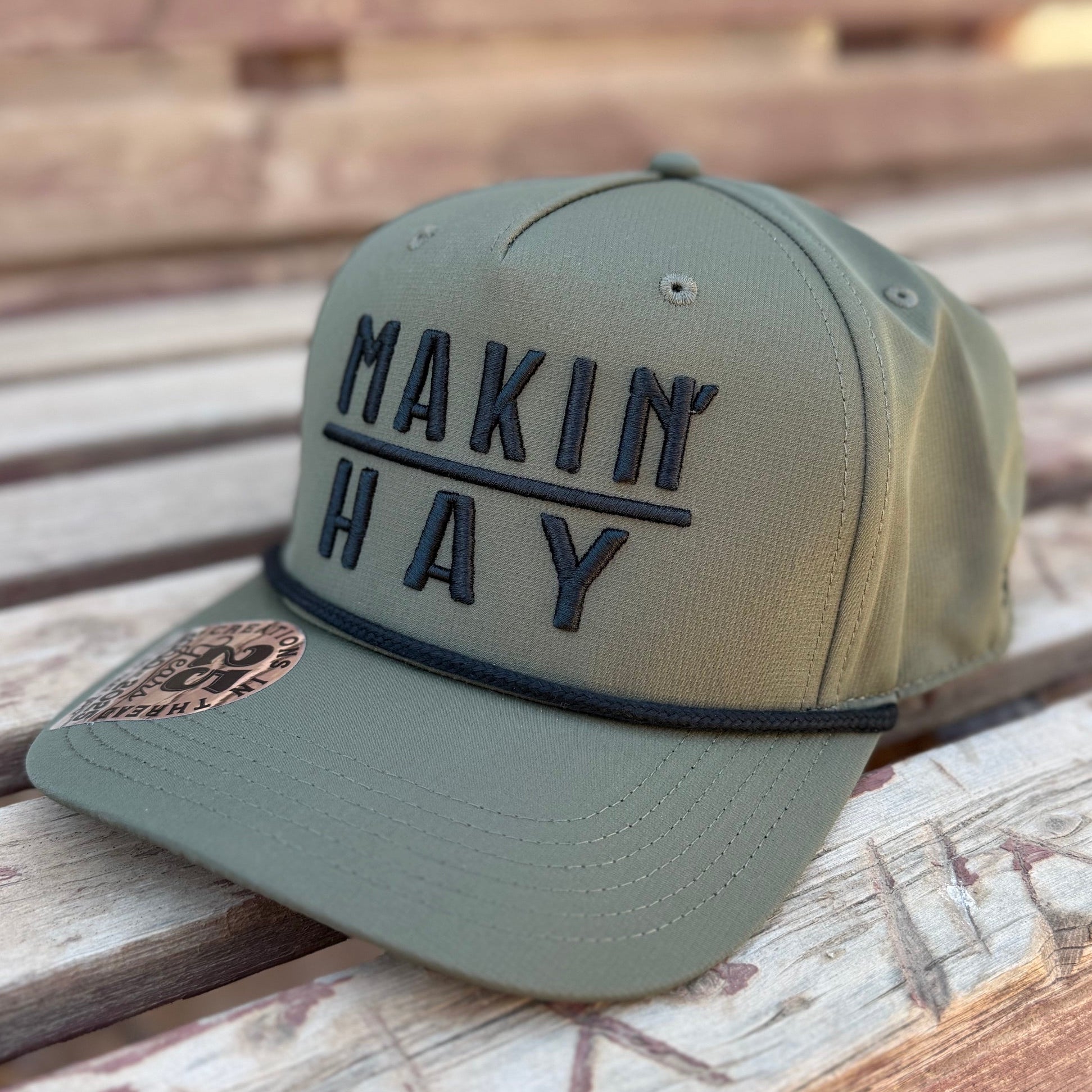 Green cap with 'MAKIN HAY' text on a wooden surface