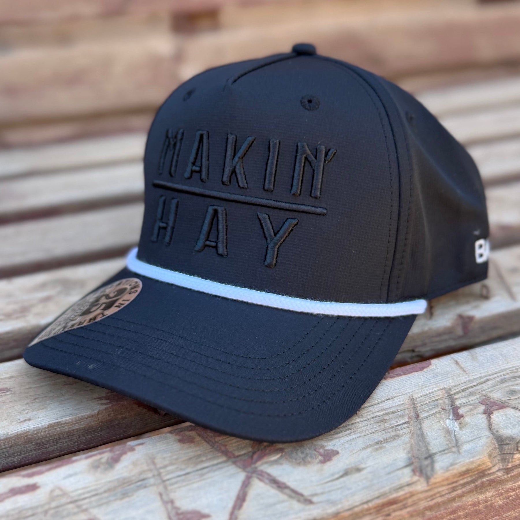 Black cap with 'MAKIN HAY' text on a wooden surface