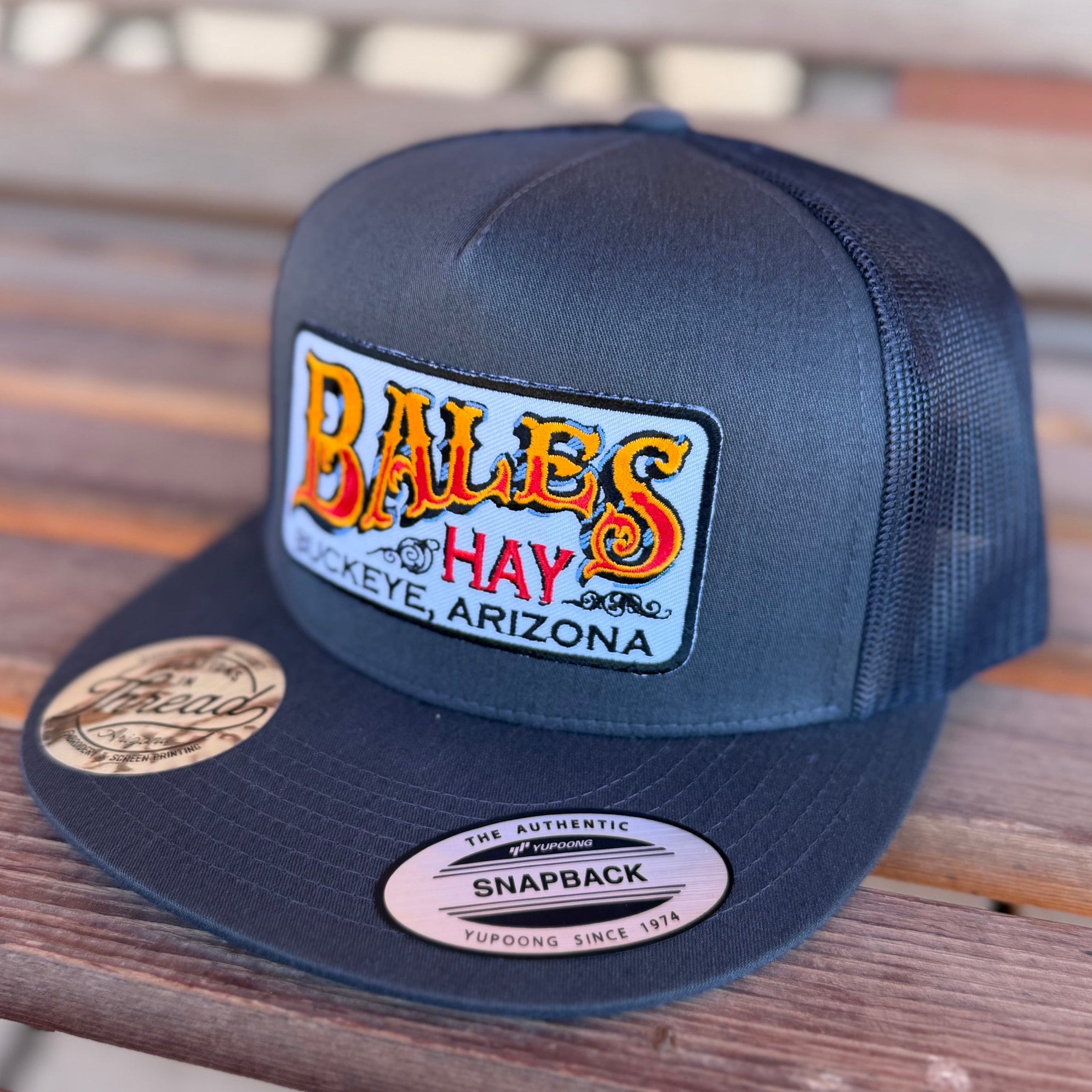 Navy blue cap with 'Bales Hay' logo on a wooden surface