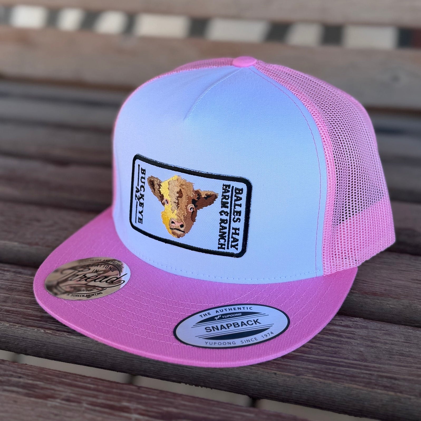 Pink and white trucker hat with a logo on a wooden surface