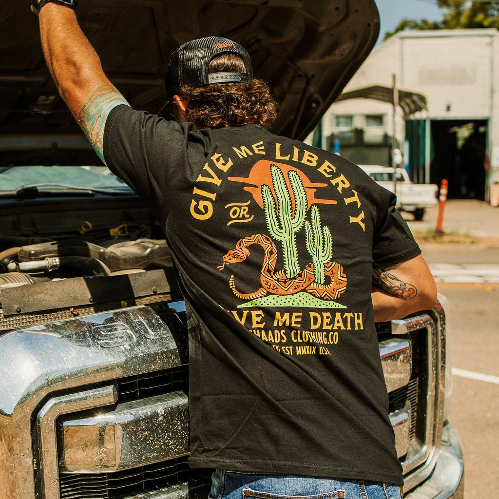 Person wearing a black t-shirt with a graphic design and text, standing next to an open truck hood.